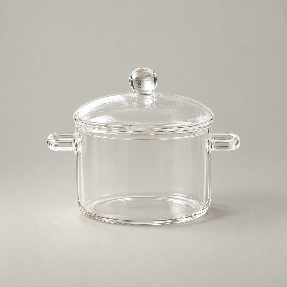Clear borosilicate glass cooking pot with a domed lid, ball knob and two loop handles on a grey background