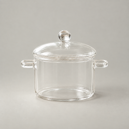 Clear borosilicate glass cooking pot with a domed lid, ball knob and two loop handles on a grey background