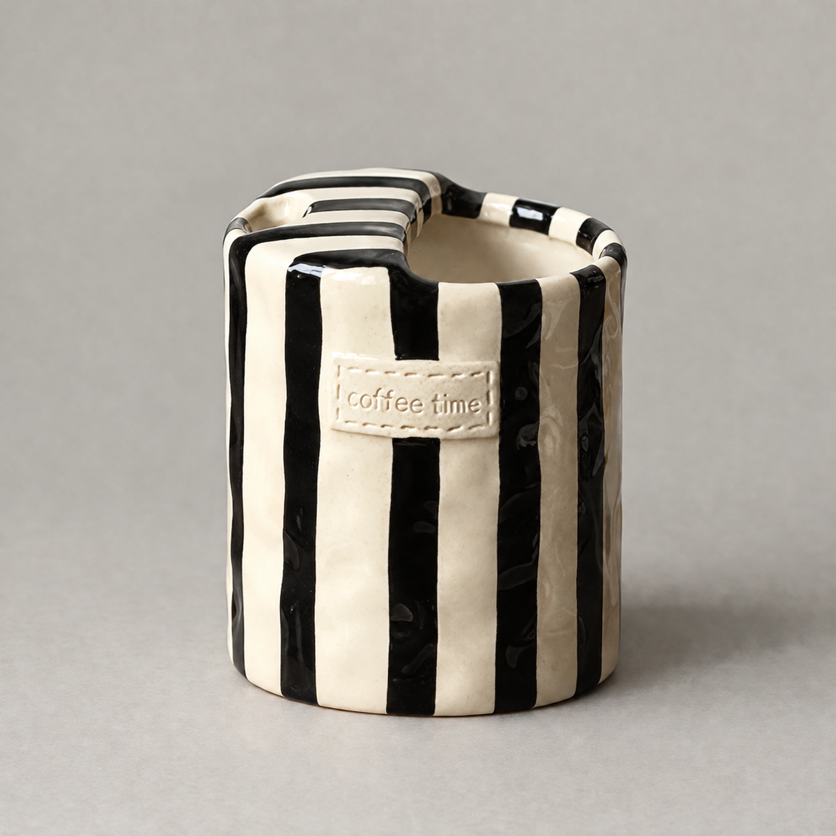Black striped handleless ceramic cup with a coffee time label on a plain grey background