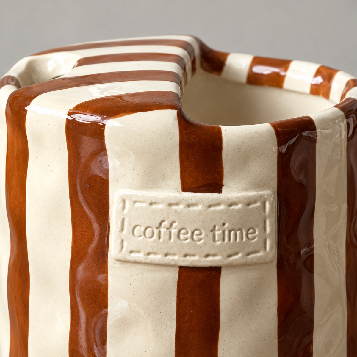 Raised coffee time label with stitched edge on a brown striped ceramic cup, close up