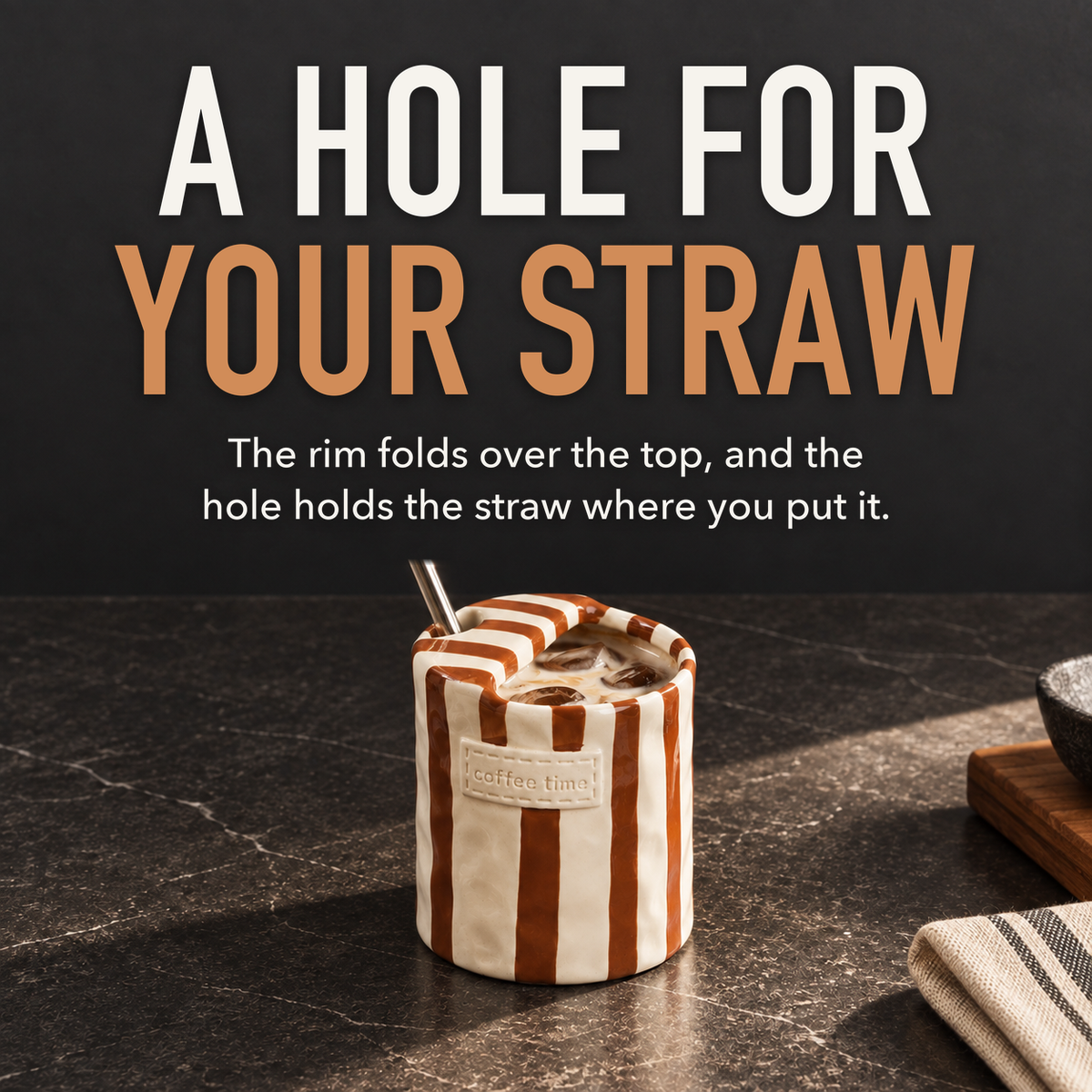 Brown striped ceramic cup of iced coffee with a steel straw standing in the round hole in its folded top, with the words A Hole For Your Straw