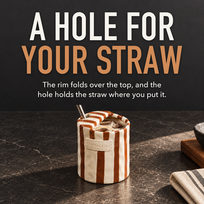 Brown striped ceramic cup of iced coffee with a steel straw standing in the round hole in its folded top, with the words A Hole For Your Straw