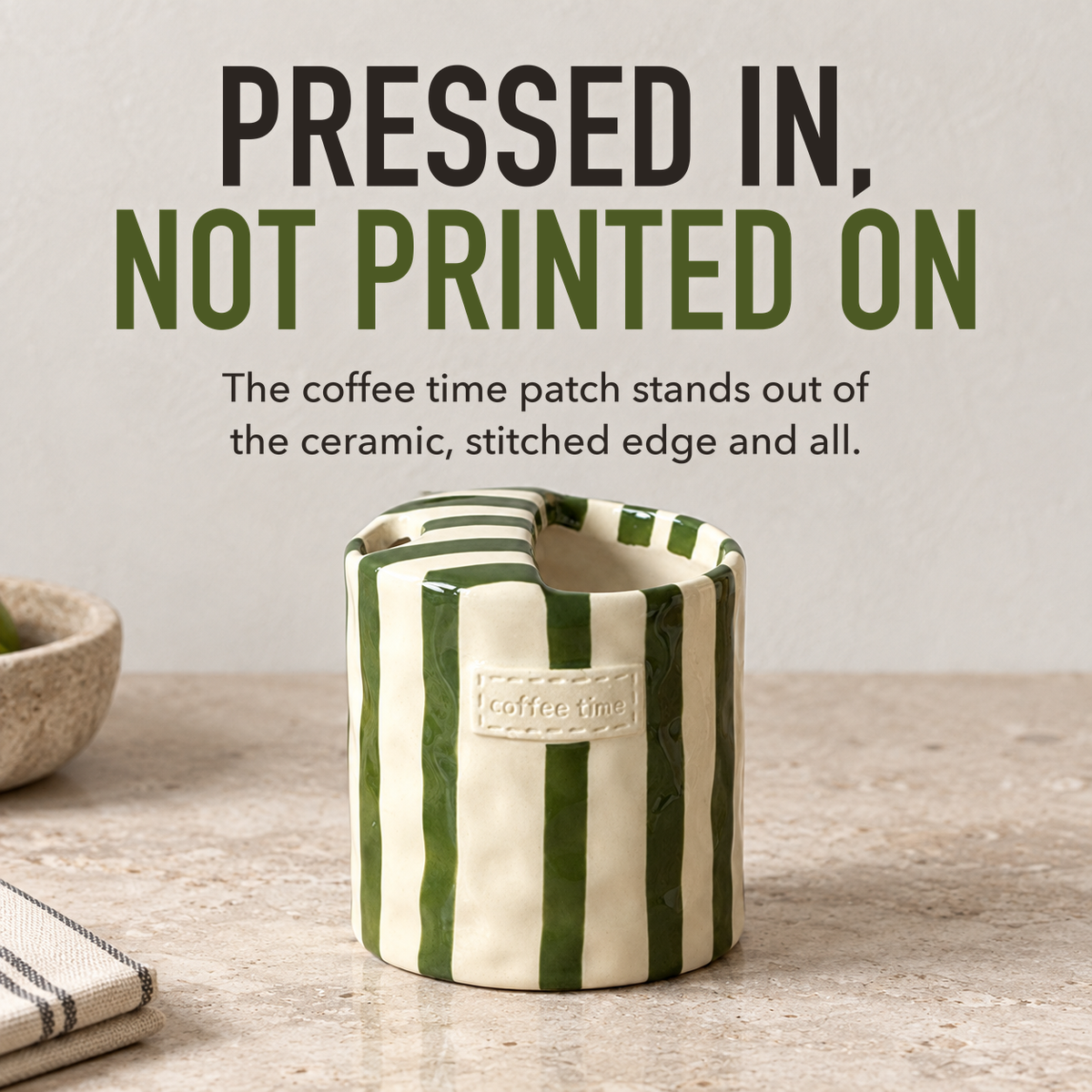 Green striped ceramic cup on a pale kitchen worktop, its raised coffee time label in close view, with the words Pressed In, Not Printed On