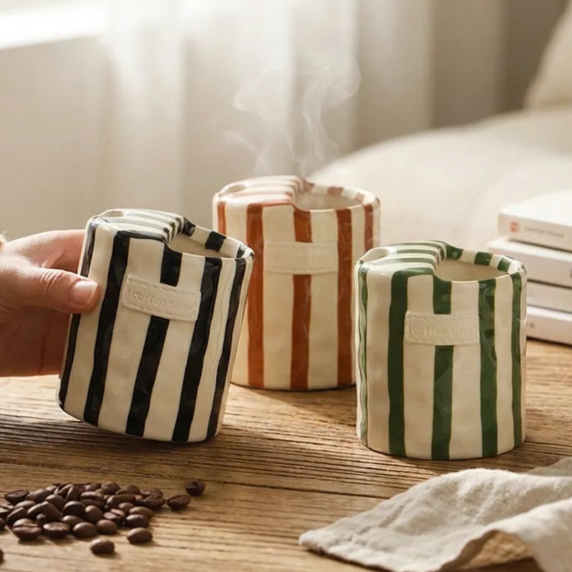 Black, brown and green striped ceramic cups on a wooden table beside coffee beans and a stack of books