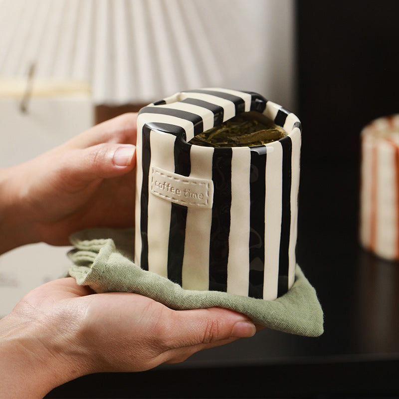 Black striped ceramic cup of loose leaf tea held on a green linen cloth