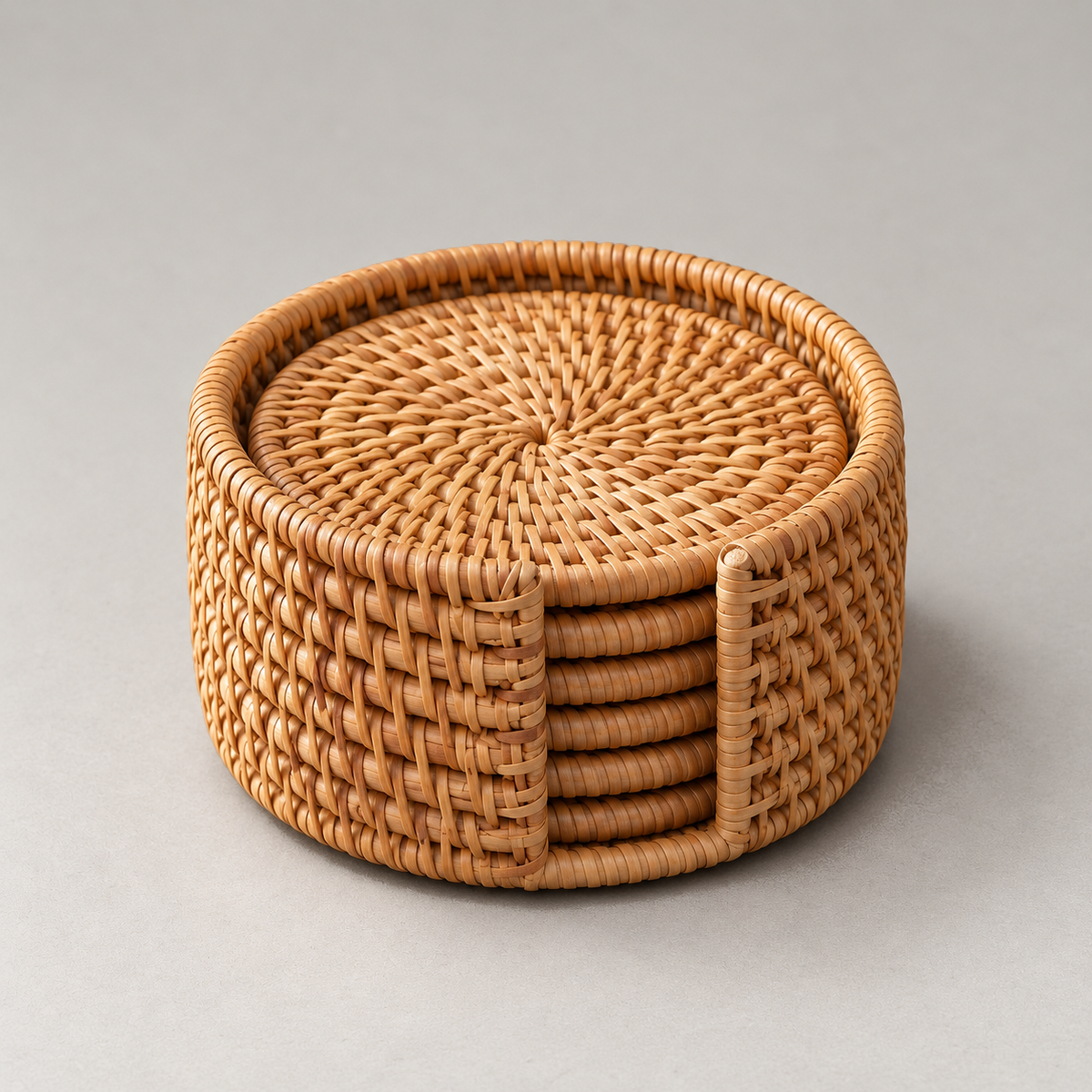 Round woven rattan coaster holder with six stacked coasters showing through the slot in its side, on a plain grey background