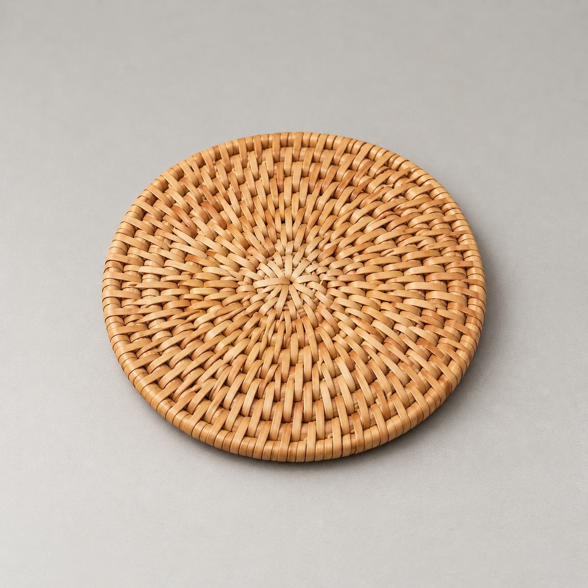 Close view of one round rattan coaster showing the sunburst weave radiating from its center to a wrapped border
