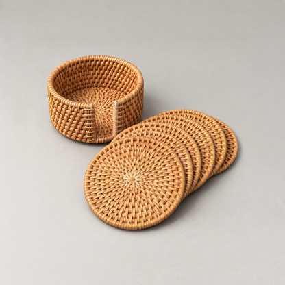 Everything in the set: an empty round rattan coaster holder and six woven rattan coasters fanned out beside it on grey
