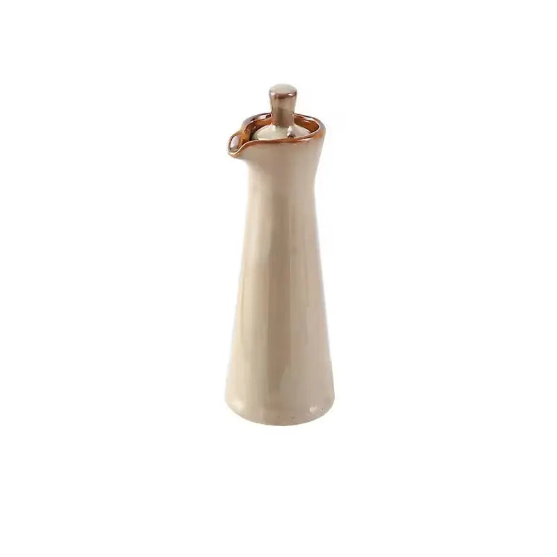 Beige ceramic oil dispenser with a rust brown rim and matching glazed stopper, standing alone on a white background