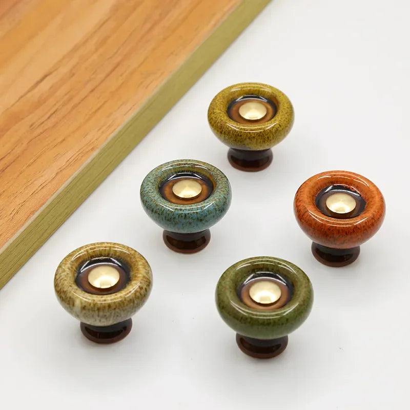 Five speckled ceramic cabinet knobs in the flared style, in green, teal, mustard, orange and beige, each with a gold-tone center cap