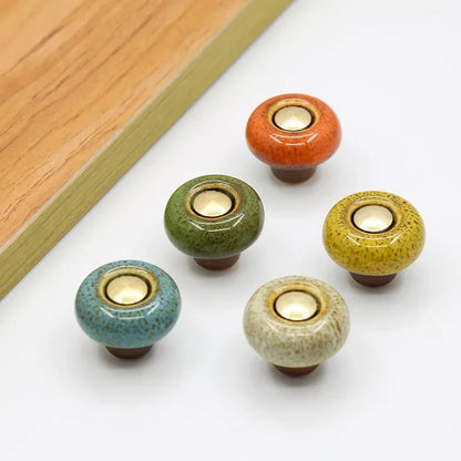 Five speckled ceramic cabinet knobs in the round style, in orange, green, mustard, teal and beige, each with a gold-tone center cap