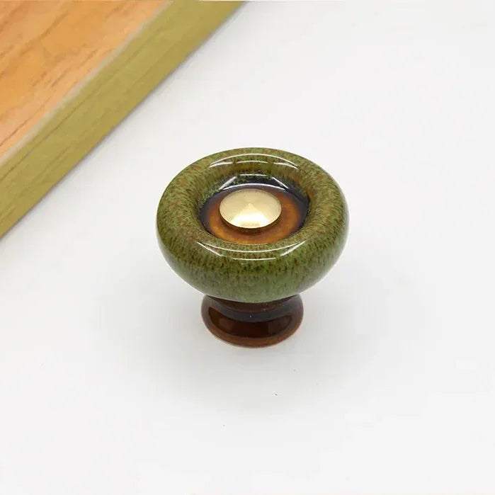 Green speckled ceramic cabinet knob with a flared dark brown foot and a dark glaze ring around its gold-tone center cap