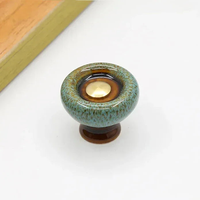 Teal speckled ceramic cabinet knob with a flared dark brown foot and a dark glaze ring around its gold-tone center cap