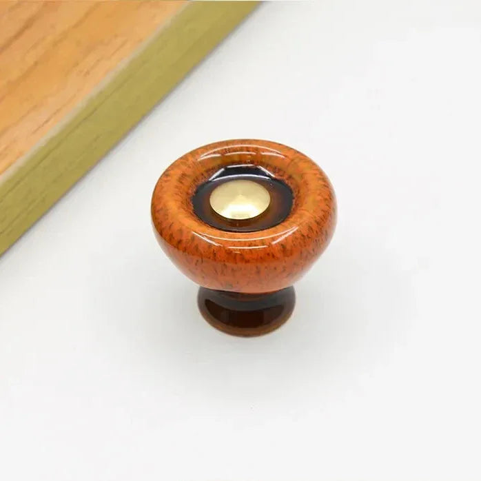 Orange speckled ceramic cabinet knob with a flared dark brown foot and a dark glaze ring around its gold-tone center cap