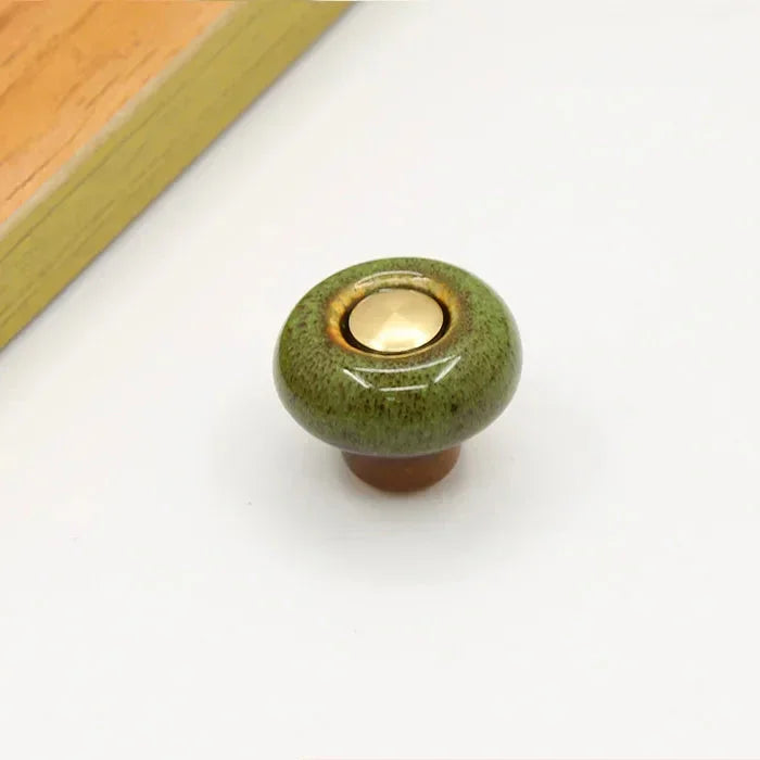 Green speckled ceramic cabinet knob in the round style, with a short brown stem and a gold-tone center cap