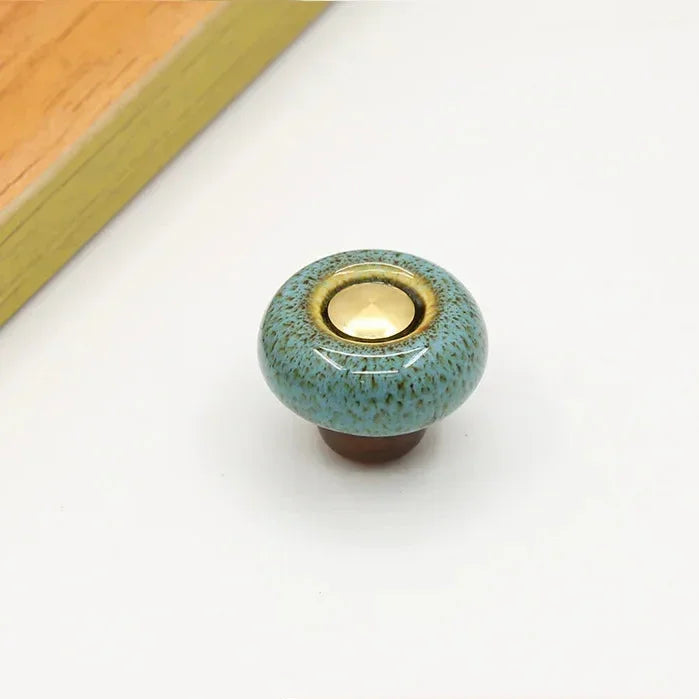 Teal speckled ceramic cabinet knob in the round style, with a short brown stem and a gold-tone center cap