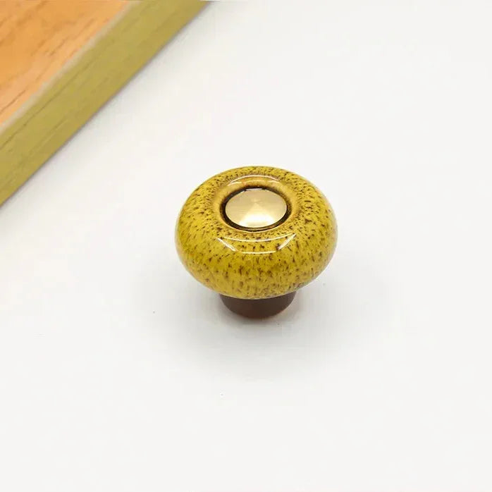 Mustard speckled ceramic cabinet knob in the round style, with a short brown stem and a gold-tone center cap