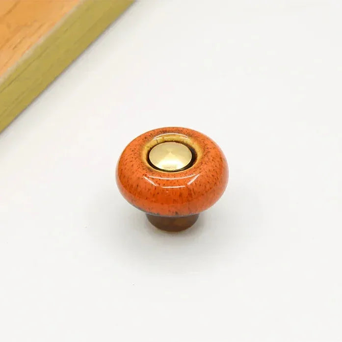 Orange speckled ceramic cabinet knob in the round style, with a short brown stem and a gold-tone center cap