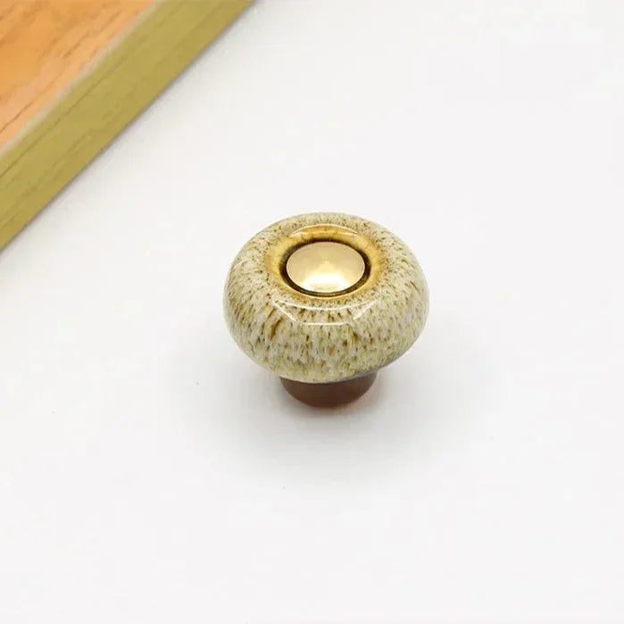 Beige speckled ceramic cabinet knob in the round style, with a short brown stem and a gold-tone center cap