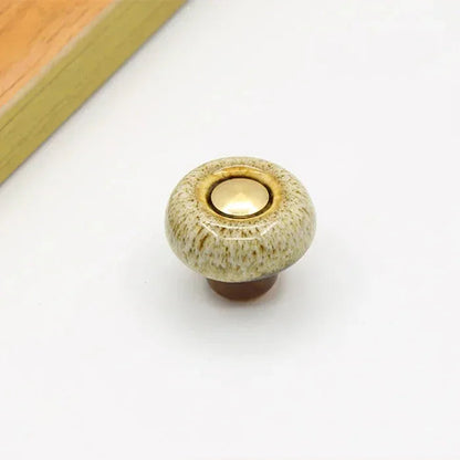 Beige speckled ceramic cabinet knob in the round style, with a short brown stem and a gold-tone center cap