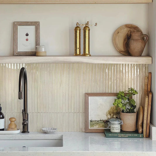 Pale wood grain strip tiles as a kitchen sink backsplash below an open oak shelf, with a black faucet and a white stone counter