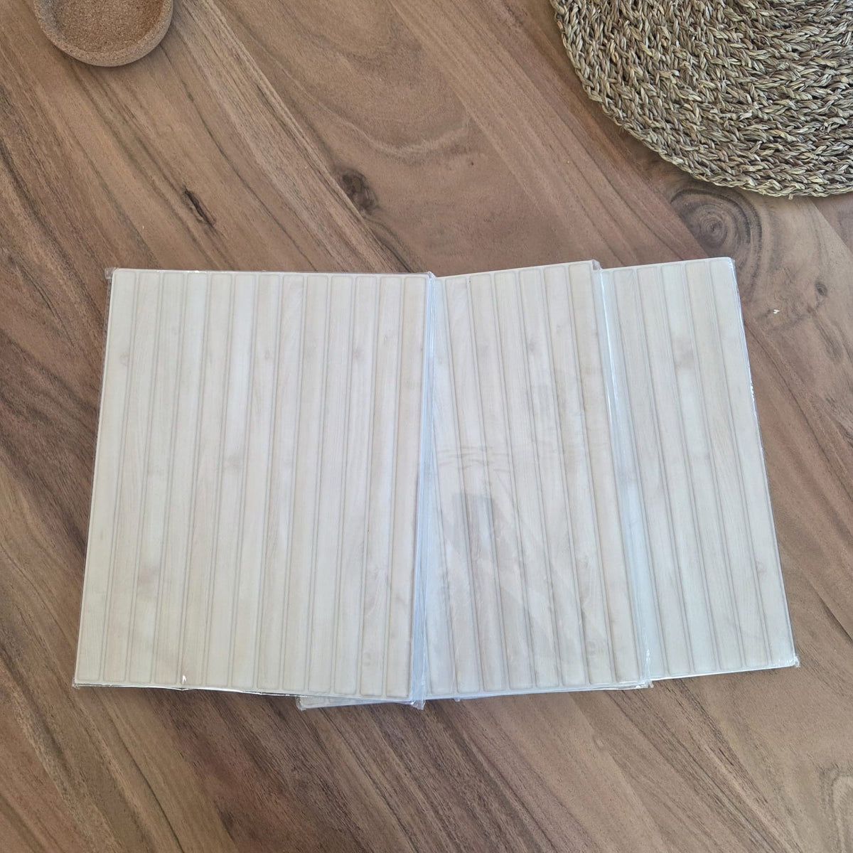 Three peel and stick tile sheets in clear plastic sleeves on a walnut table