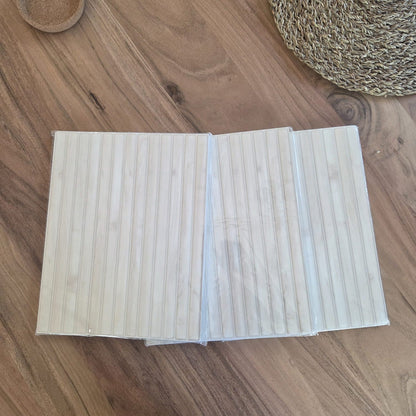 Three peel and stick tile sheets in clear plastic sleeves on a walnut table