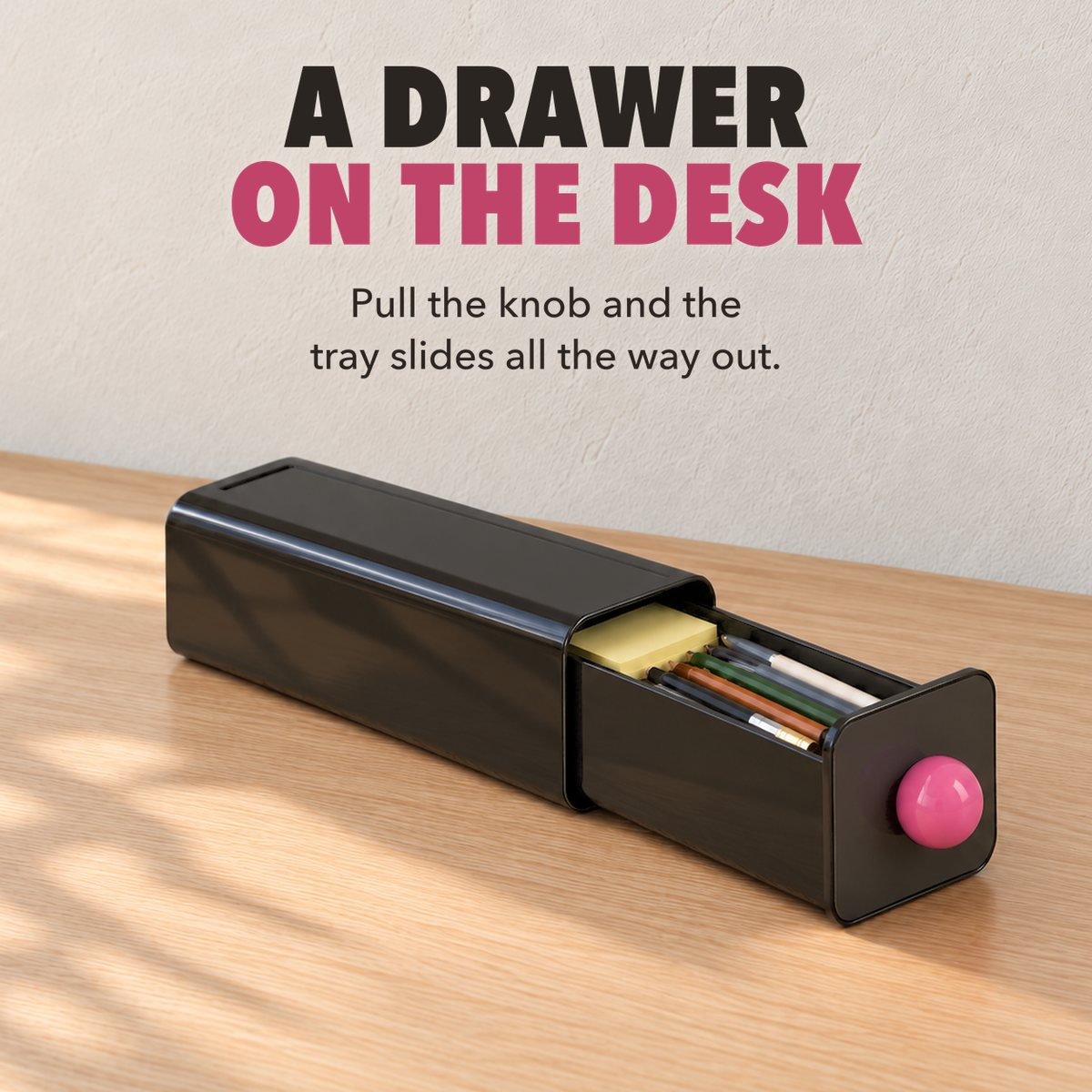 Black storage drawer pulled halfway out on a desk with pens inside, with the words A drawer on the desk