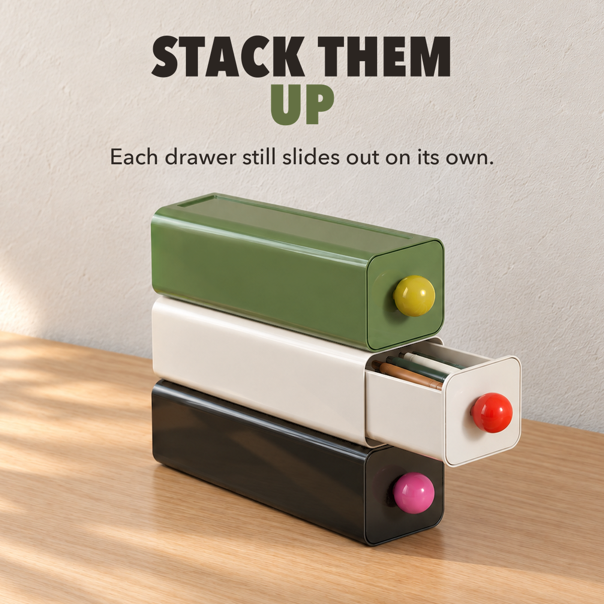 Black, white and green storage drawers stacked on a desk with the middle drawer open, with the words Stack them up