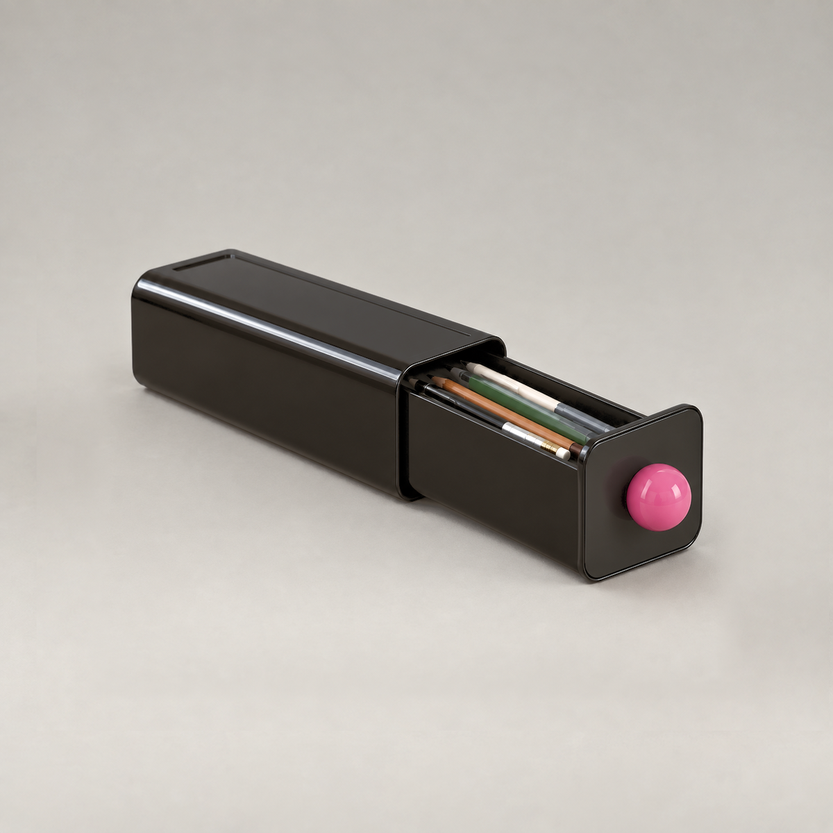 Black storage drawer on a grey background with its tray pulled halfway out holding pens and pencils