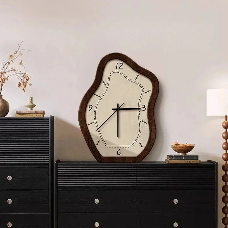Wavy wall clock with a wood-grain frame and a cream face standing on a black sideboard beside a vase of dried stems
