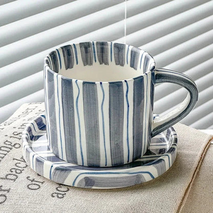 Slate blue striped ceramic cup with thin blue lines on its matching saucer, by a window with blinds