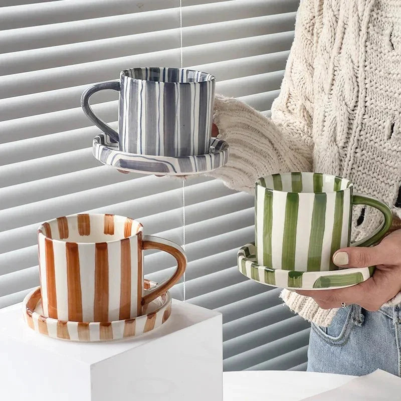 Blue, brown and green striped cups on saucers, two held up and one on a white stand