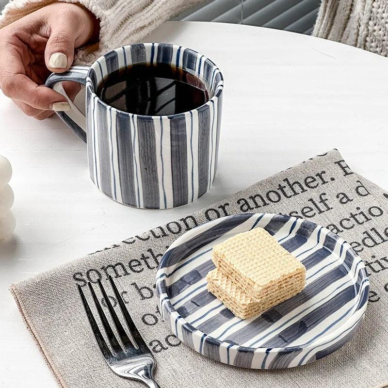 Slate blue striped cup of black coffee beside its saucer holding wafers on a linen mat