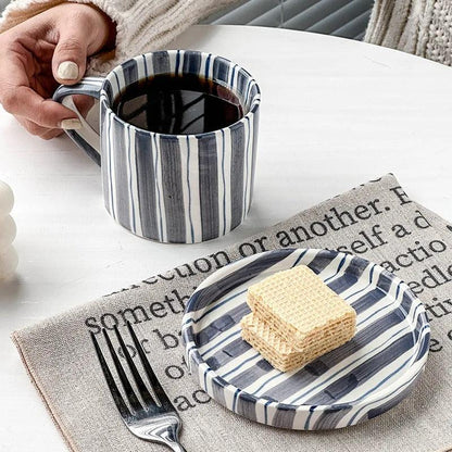 Slate blue striped cup of black coffee beside its saucer holding wafers on a linen mat