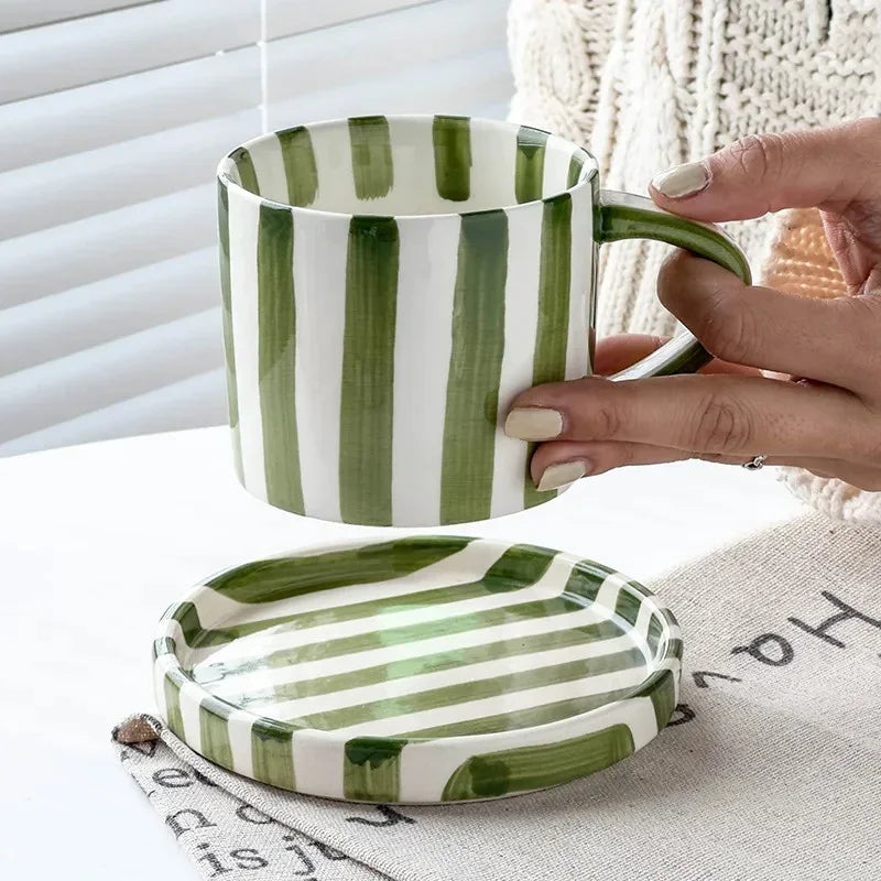 Olive green striped cup lifted above its empty striped saucer
