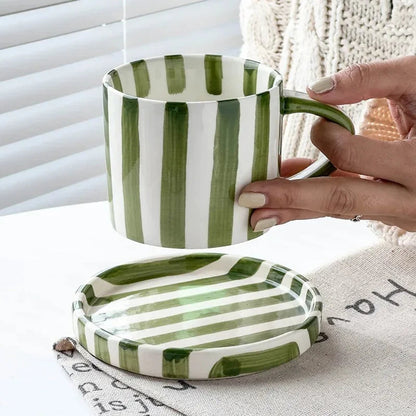Olive green striped cup lifted above its empty striped saucer