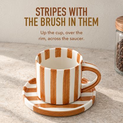 Text image: Stripes with the brush in them. An empty caramel brown striped cup on its saucer, stripes running over the rim and across the saucer