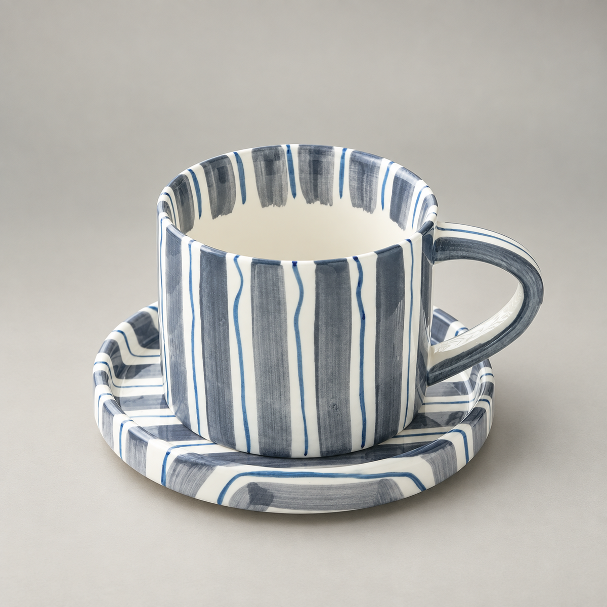 Slate blue striped ceramic cup and saucer on a plain grey background