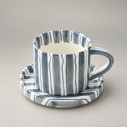 Slate blue striped ceramic cup and saucer on a plain grey background