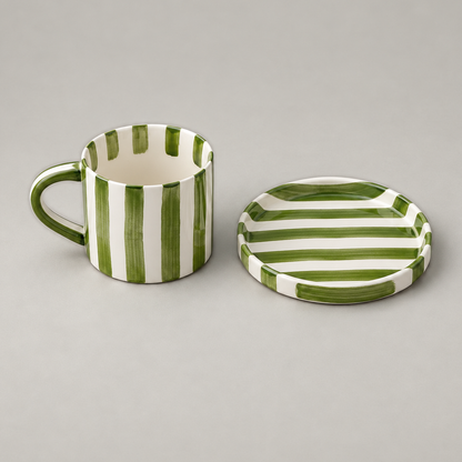 Olive green striped ceramic cup standing beside its empty flat saucer on a plain grey background