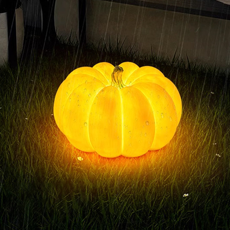 A glowing resin pumpkin lamp standing on a wet lawn in the rain, drops of water on its lit shell