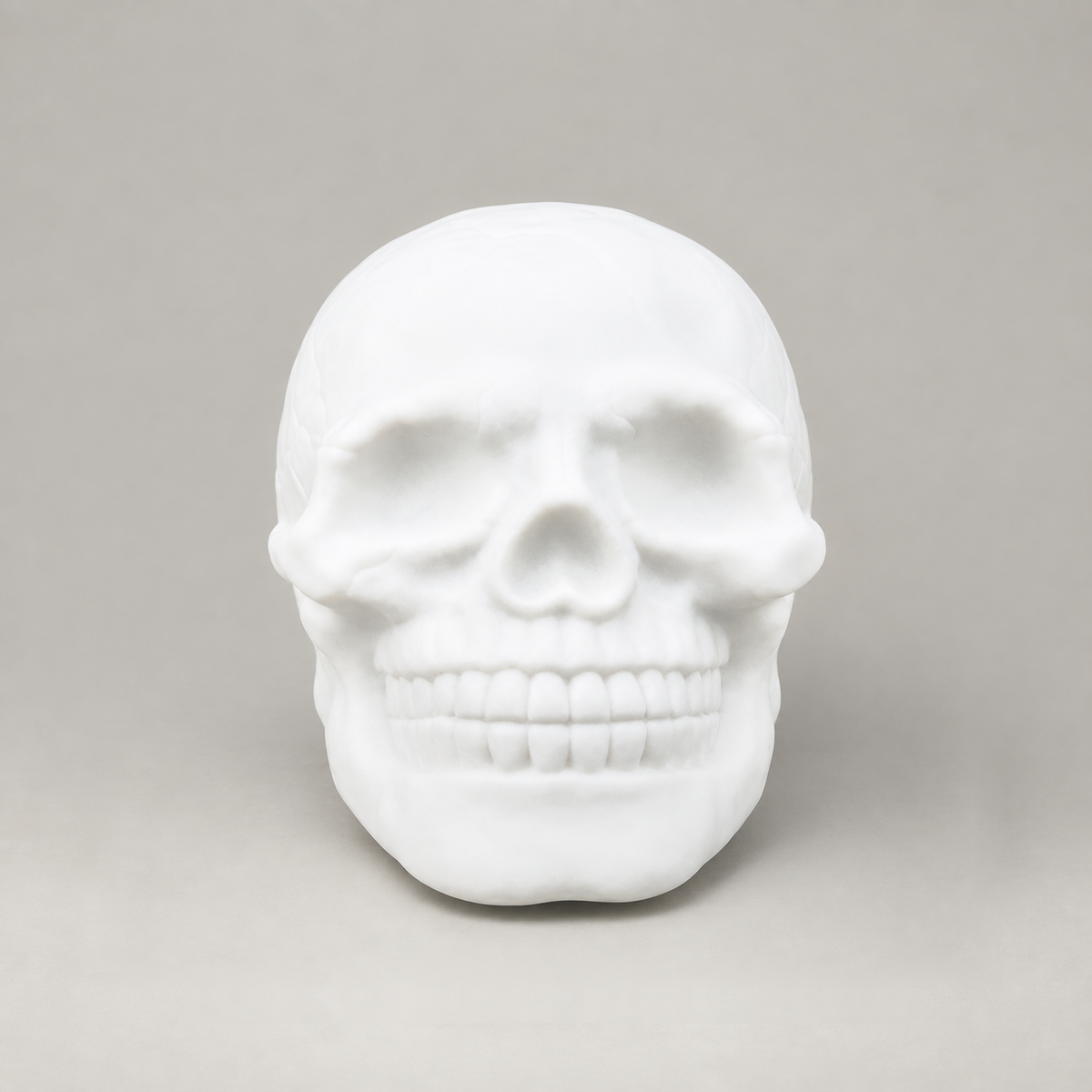 Front view of the white skull night light showing the eye sockets, nose and teeth on a grey background