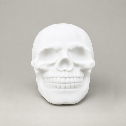 Front view of the white skull night light showing the eye sockets, nose and teeth on a grey background