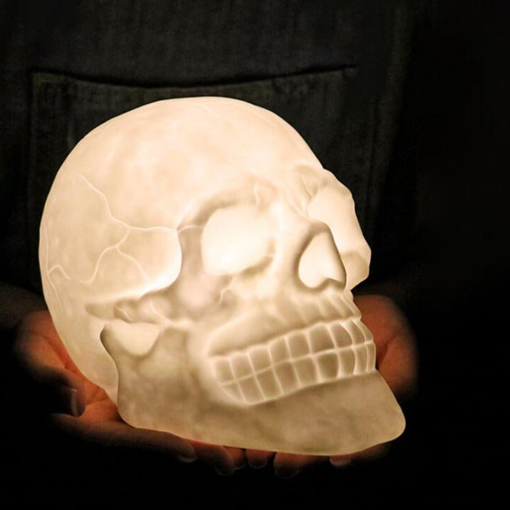 Skull night light glowing warm white, held in two hands and seen from the side