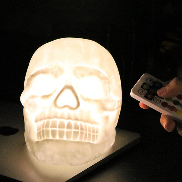 Skull night light glowing warm white on a desk while its remote control is pointed at it