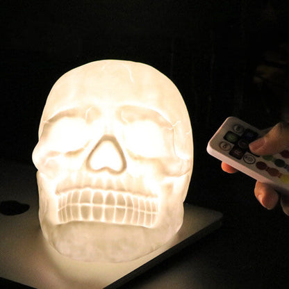Skull night light glowing warm white on a desk while its remote control is pointed at it