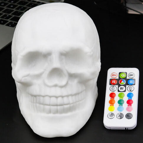 White skull night light switched off, face on, beside its remote control