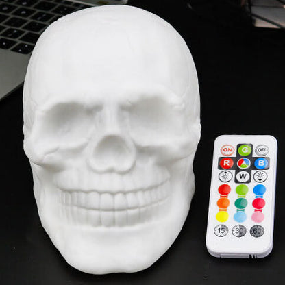 White skull night light switched off, face on, beside its remote control