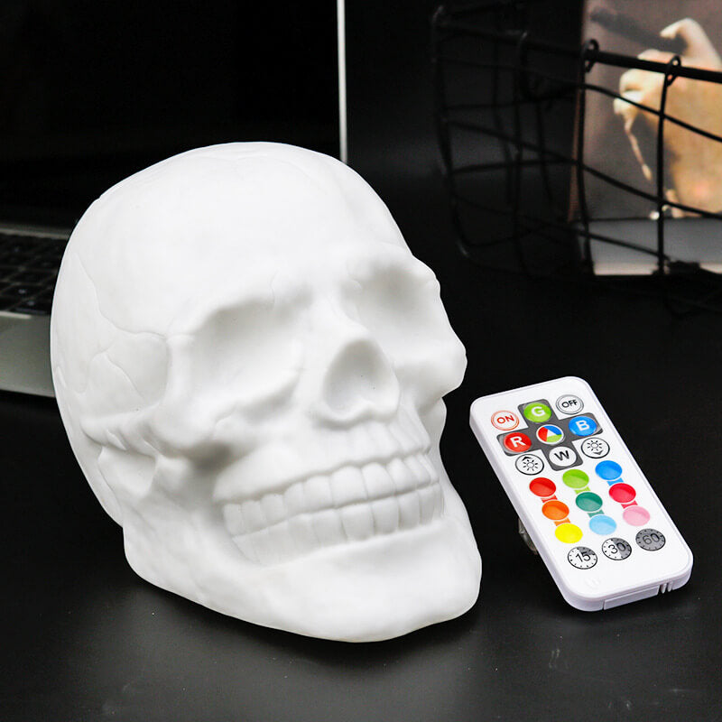 White skull night light switched off on a desk, turned three-quarters, beside its remote control